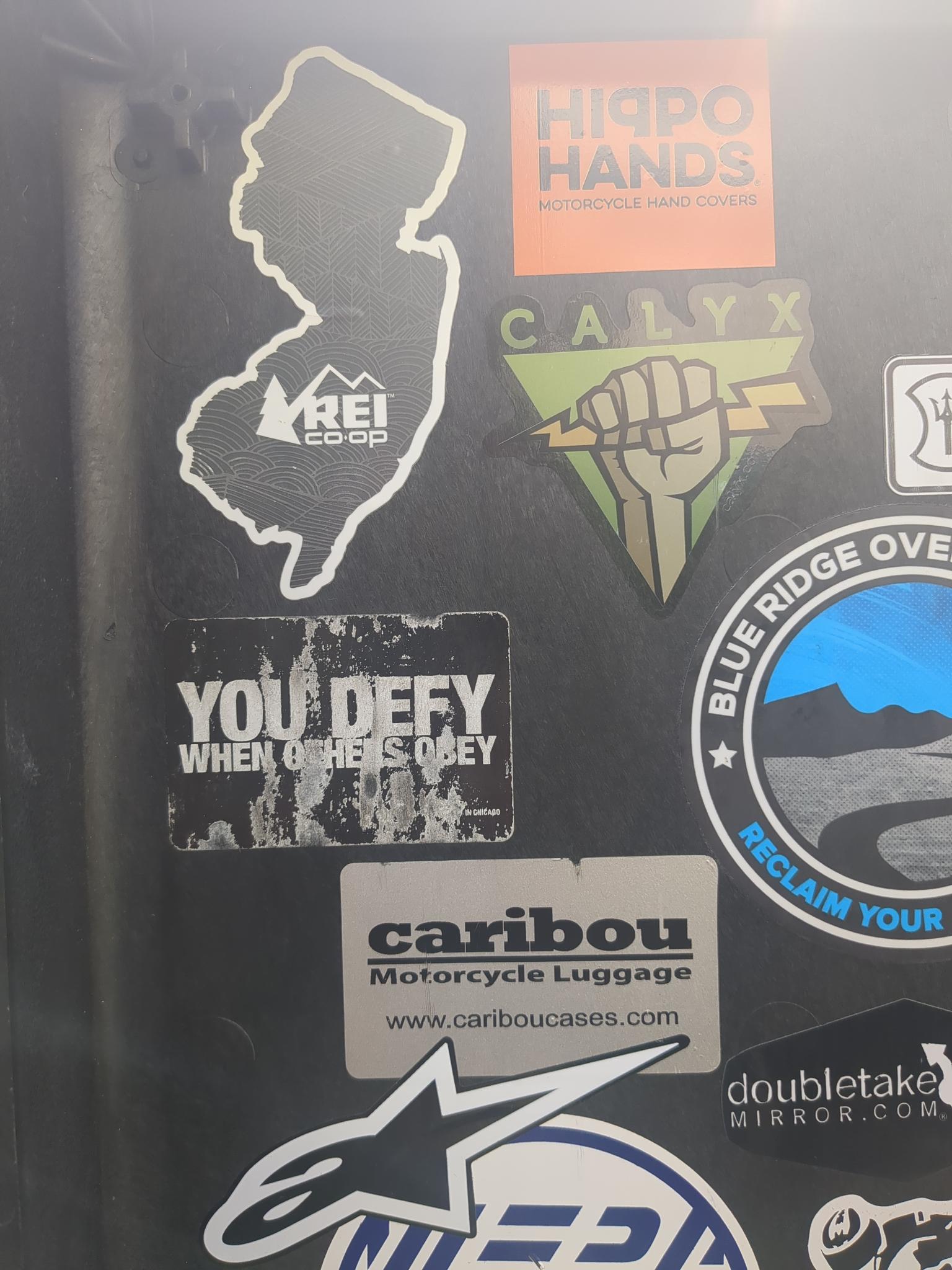 Stickes on a motorcycle top case lid, including a warn DEFY sticker